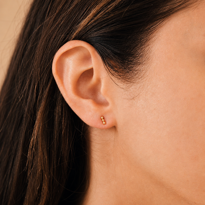 Close-up of an ear with a gold earring against a neutral background