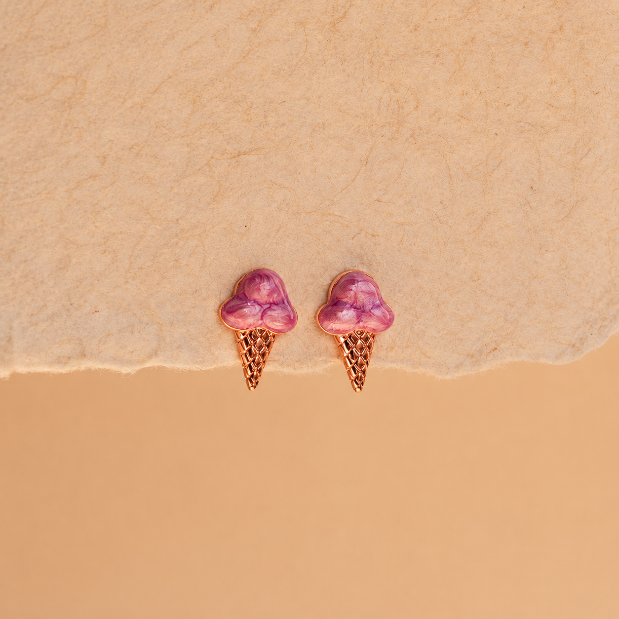 Pair of pink ice cream cone earrings on a beige background