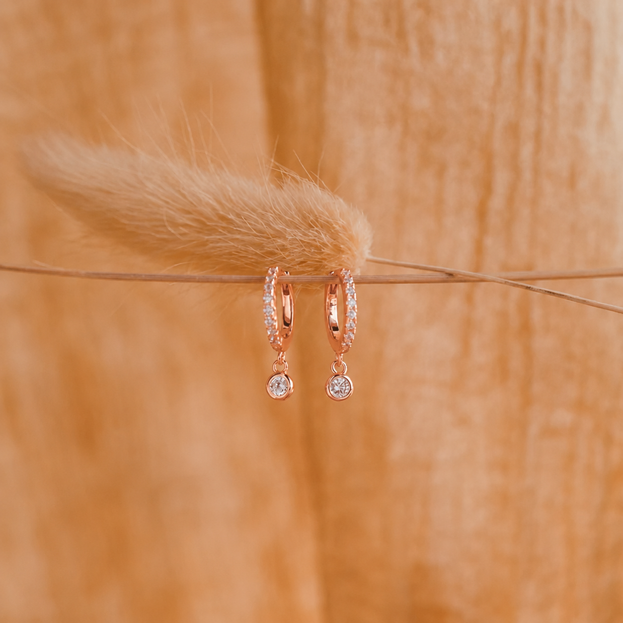 Rose gold hoop earrings with small round stones on a wooden surface with a feather.