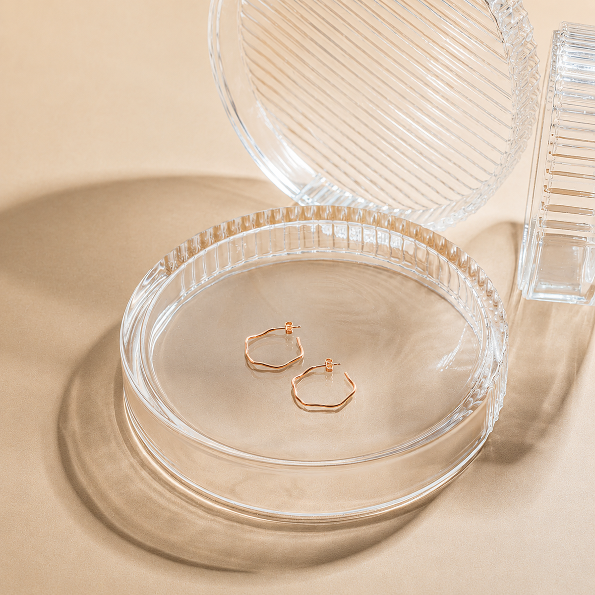 Gold hoop earrings in a clear jewelry box on a beige background