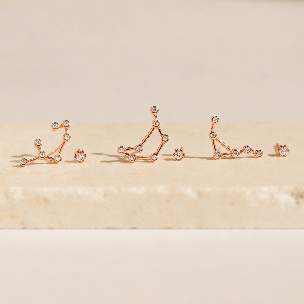 Rose gold constellation earrings on a beige background