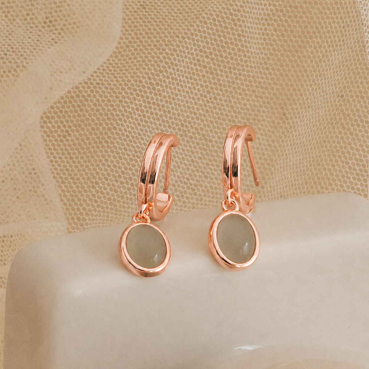 Rose gold earrings with green gemstones on a beige surface