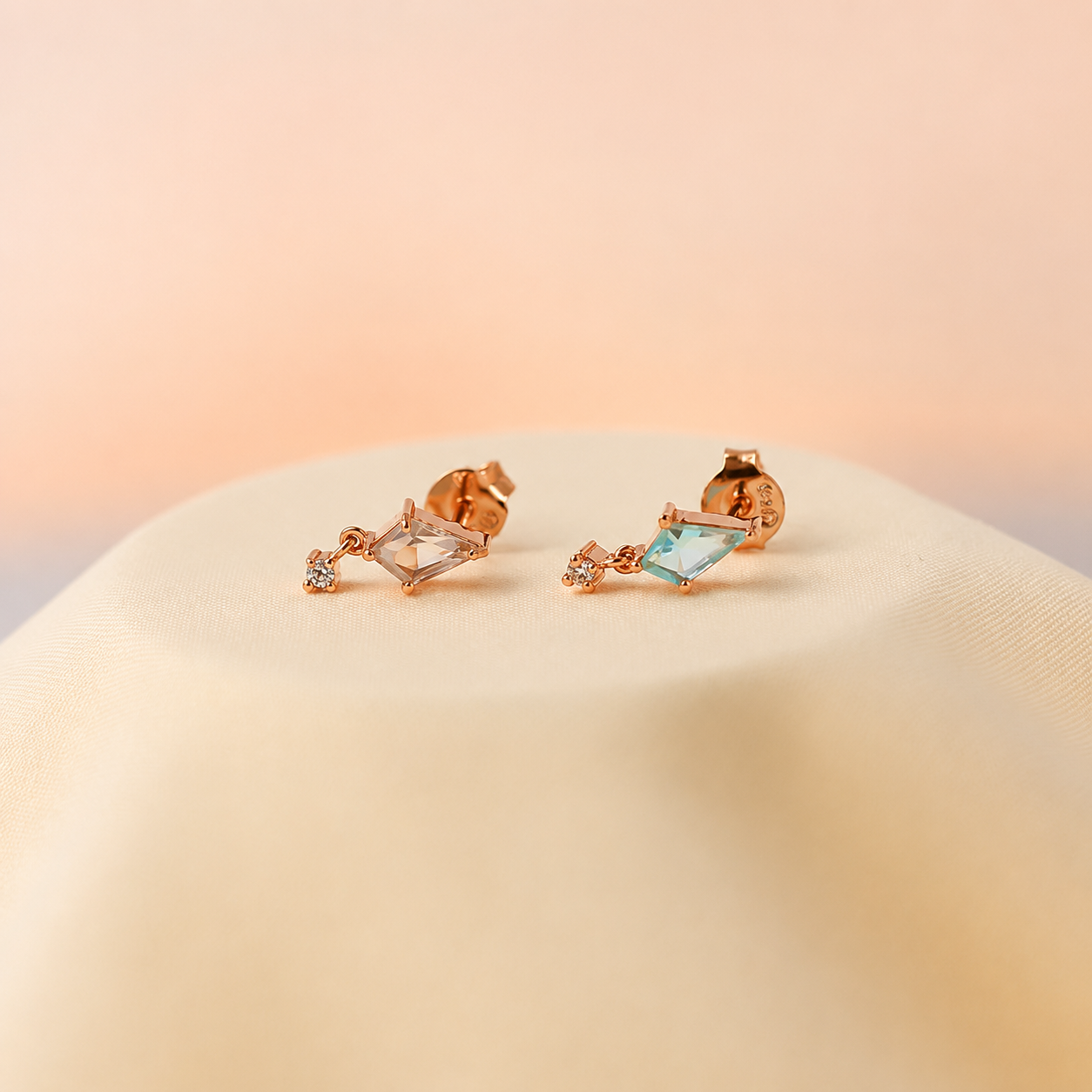 Rose gold earrings with gemstones on a beige surface