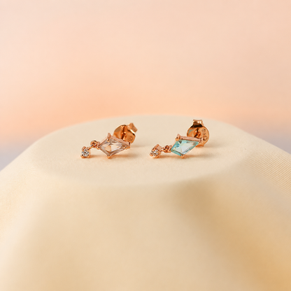 Rose gold earrings with gemstones on a beige surface