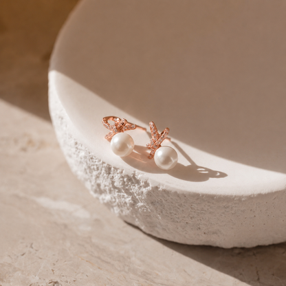 Pair of pearl earrings with rose gold settings on a textured white surface