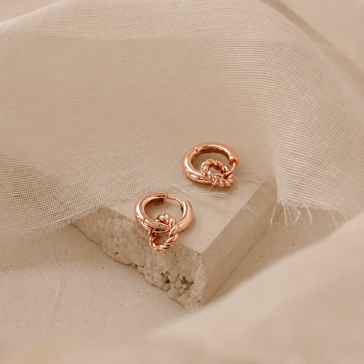 Rose gold earrings on a textured beige surface