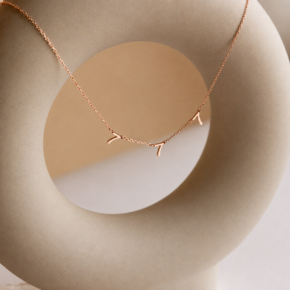 Rose gold necklace with leaf design on a beige background