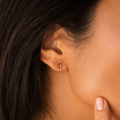 Close-up of an ear wearing a gold earring with a letter 'A' on a neutral background