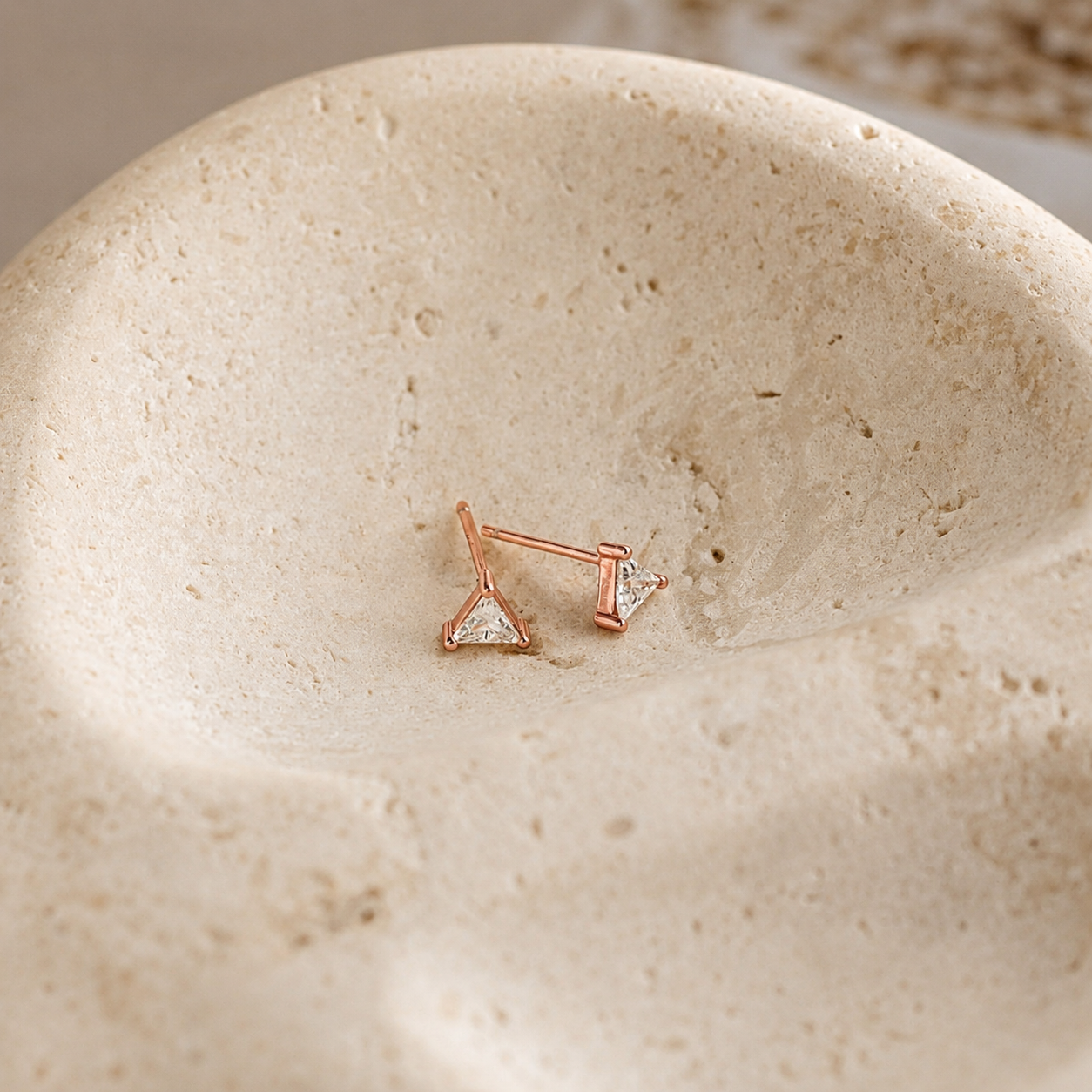 Rose gold earrings with clear gemstones on a beige stone surface