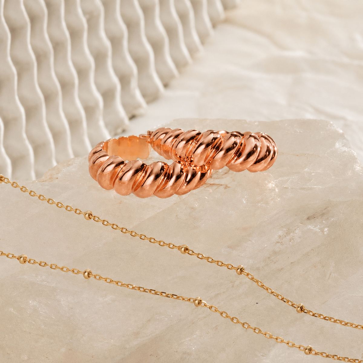 Rose gold ring and necklace on a textured beige surface