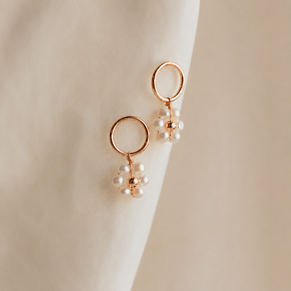 Gold hoop earrings with pearl drops on a beige background