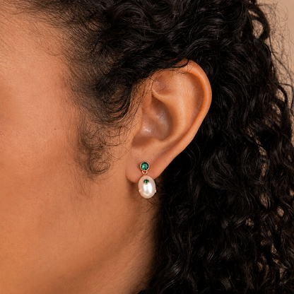 Close-up of an ear wearing a pearl earring with green gemstones.