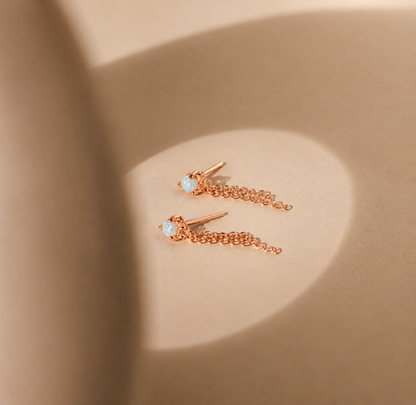 Rose gold chain earrings with gemstones on a beige background