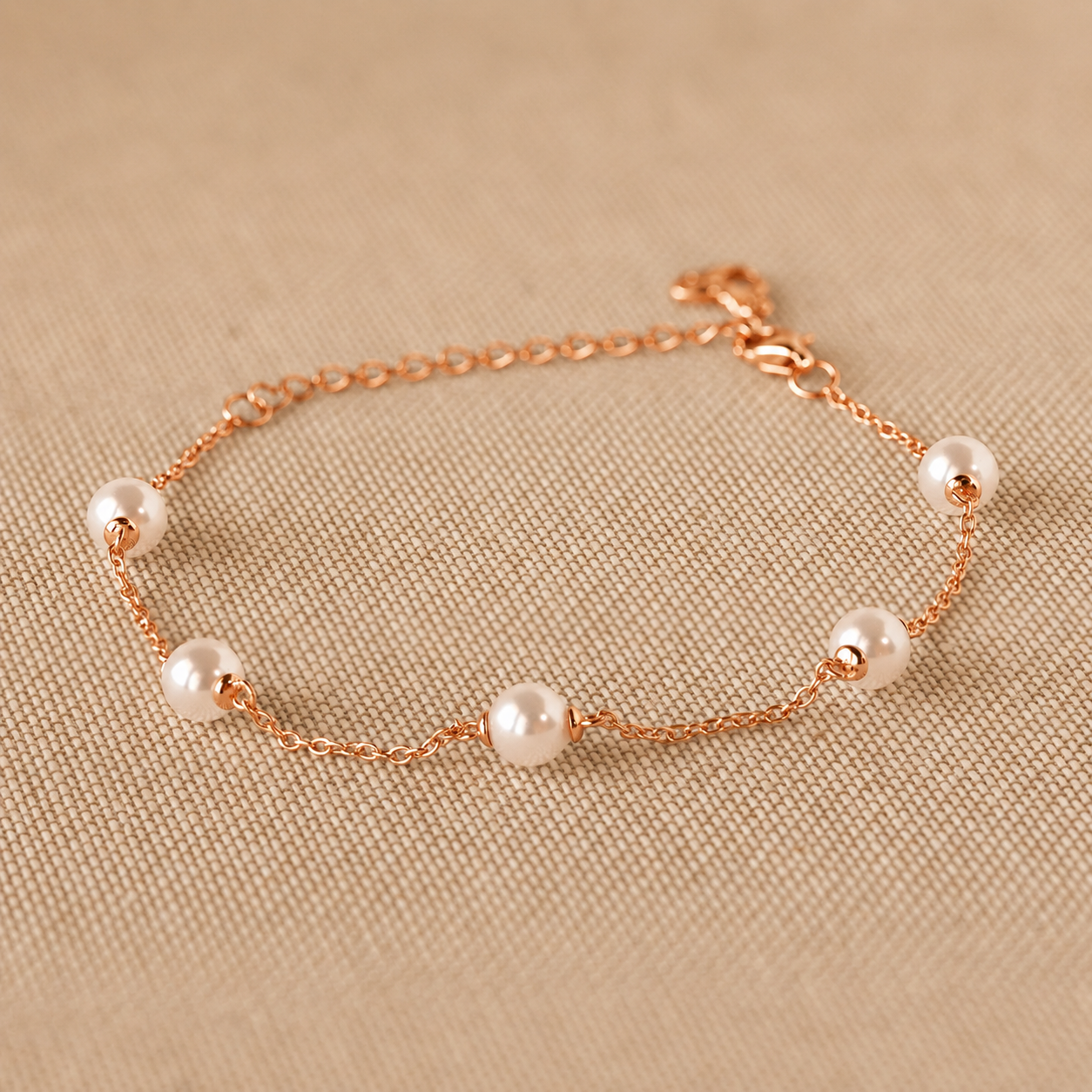 Rose gold bracelet with pearls on a beige fabric background