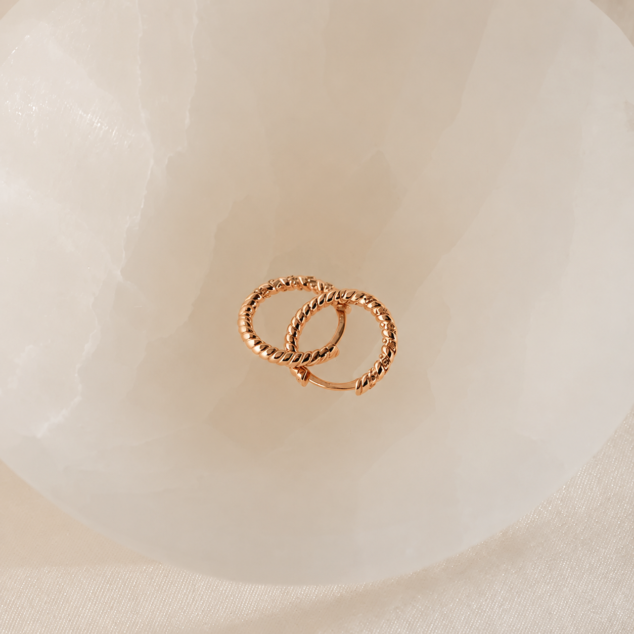 Pair of gold hoop earrings on a soft white fabric background