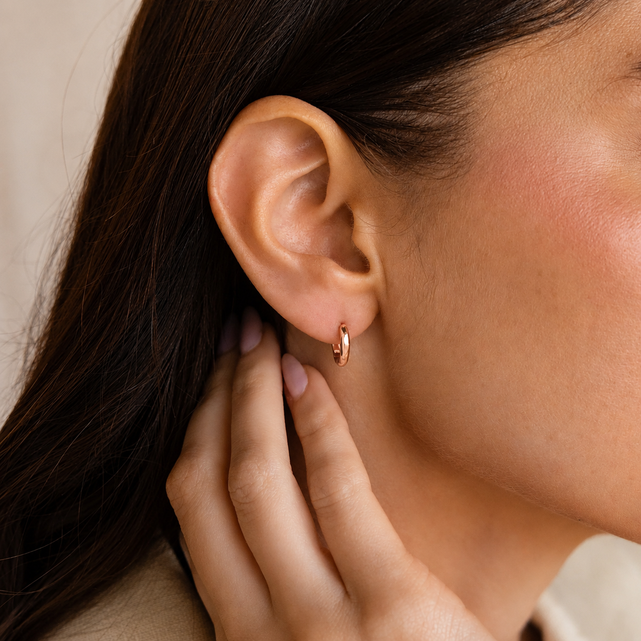 Close-up of an ear with a gold hoop earring and hand touching the earlobe.