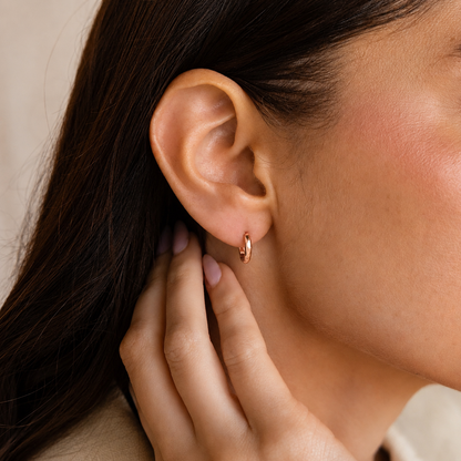 Close-up of an ear with a gold hoop earring and hand touching the earlobe.