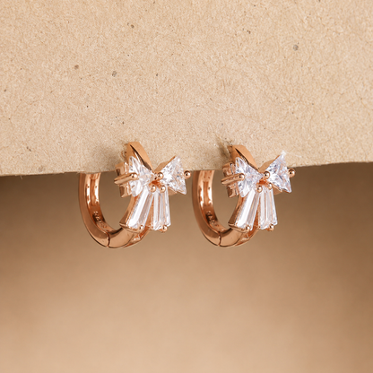 Rose gold hoop earrings with clear gemstones on a beige background