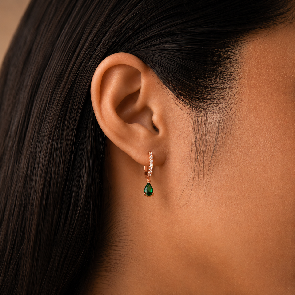 Close-up of an ear wearing a green gemstone earring with a neutral background