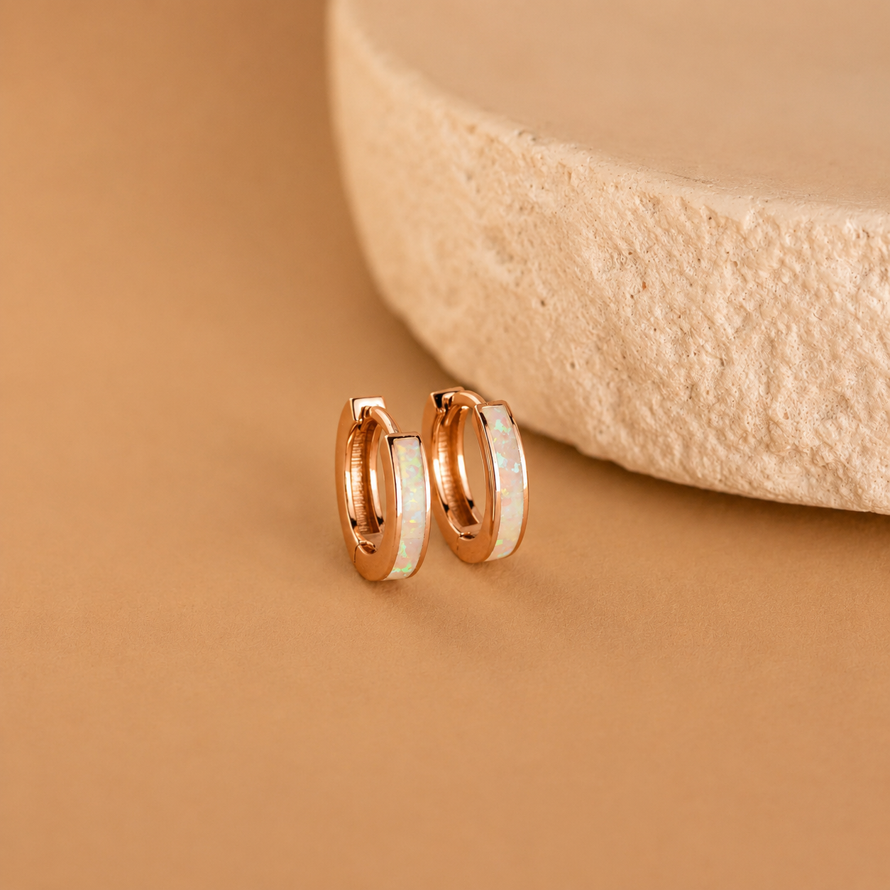 Rose gold hoop earrings on a beige stone surface