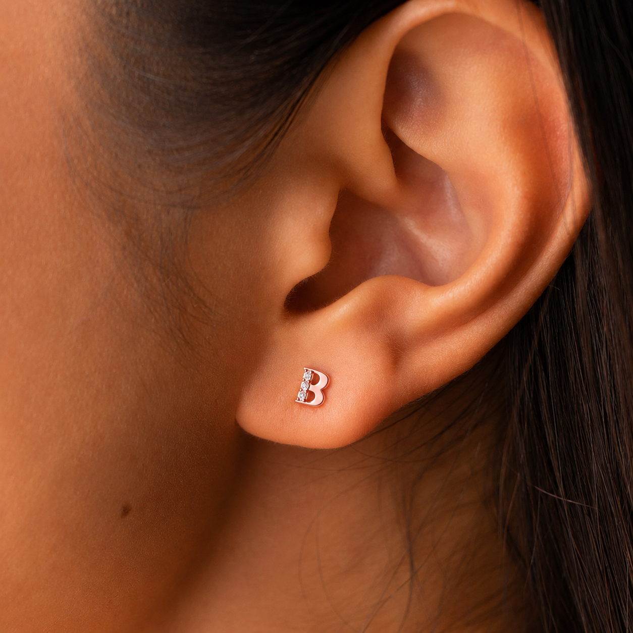 Close-up of an ear wearing a silver 'B' earring.