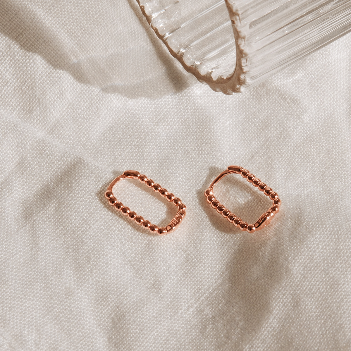 Rose gold hoop earrings on a textured beige surface with a crystal in the background