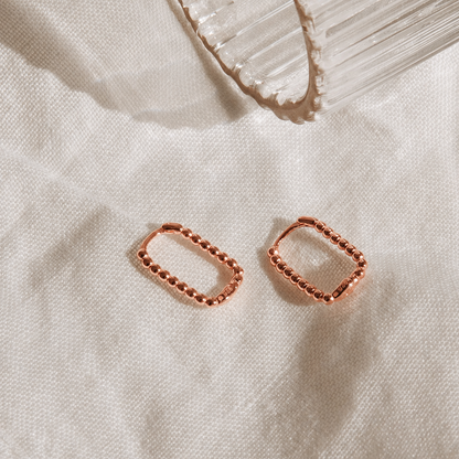 Rose gold hoop earrings on a textured beige surface with a crystal in the background