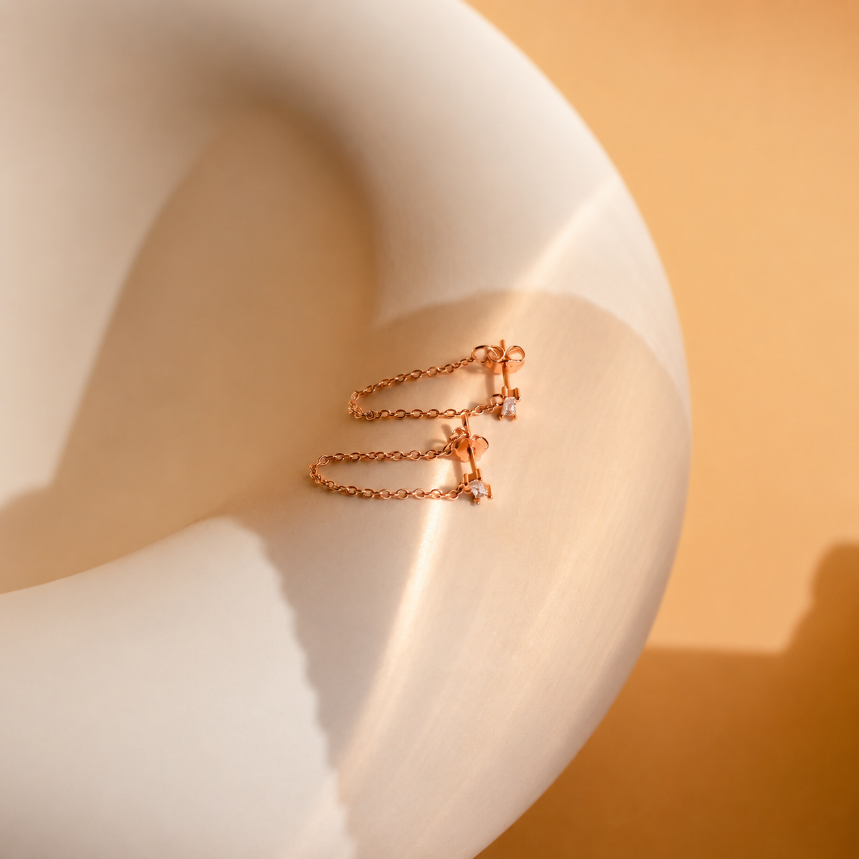 Rose gold chain earring on a mannequin ear with a warm background