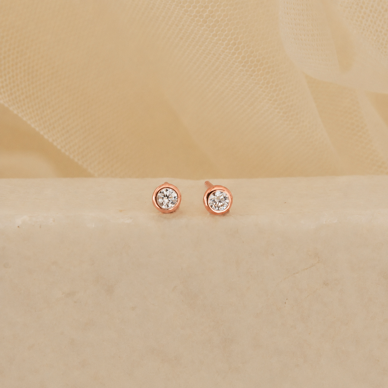 Rose gold earrings with clear gemstones on a beige fabric background
