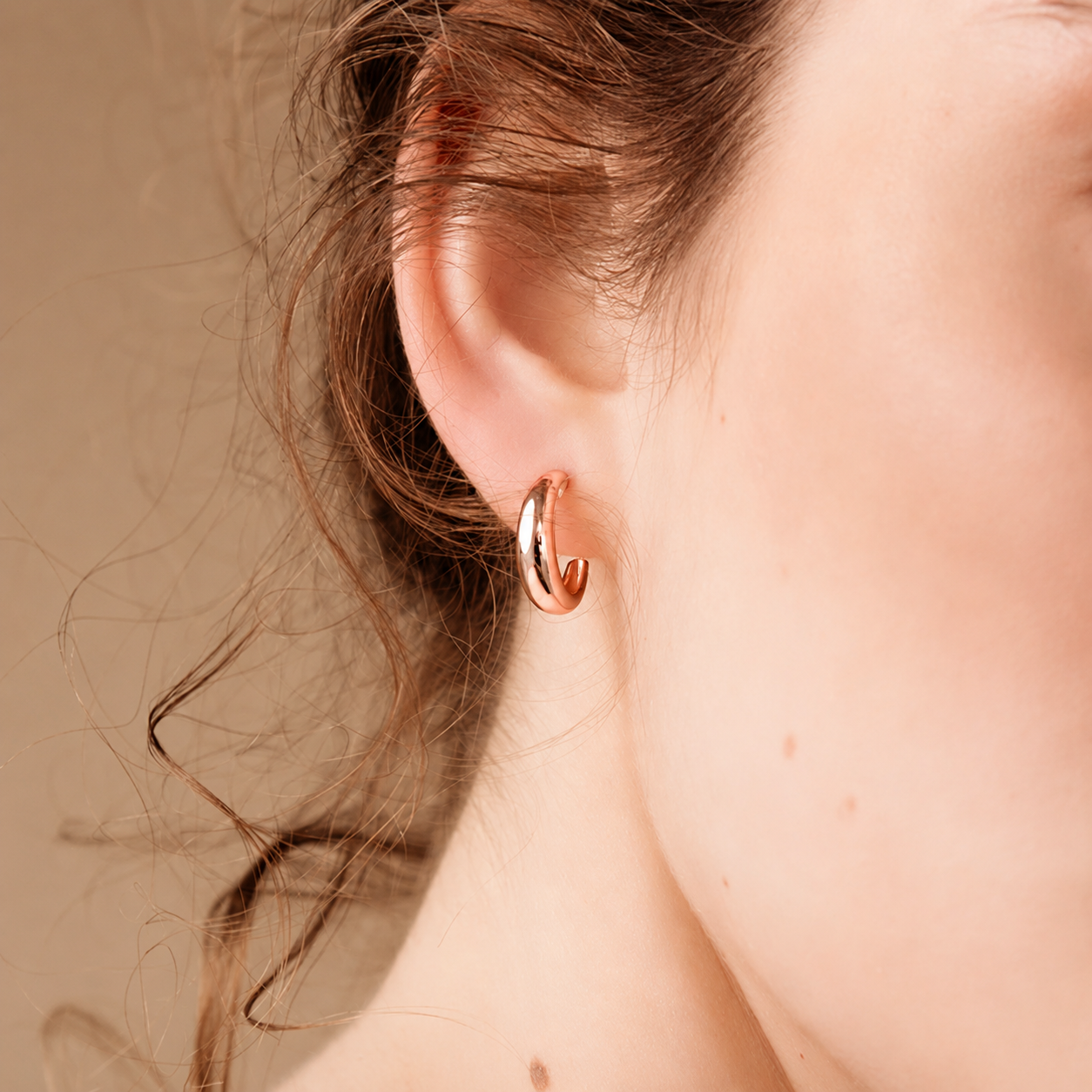 Close-up of a person wearing a rose gold hoop earring against a neutral background