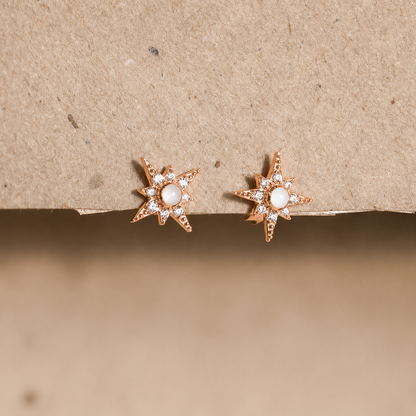 Star-shaped earrings with a central gemstone on a beige background
