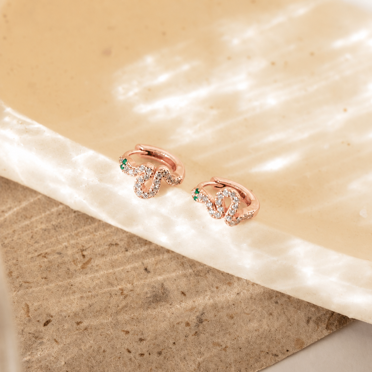 Rose gold earrings with green gemstones on a beige fabric background