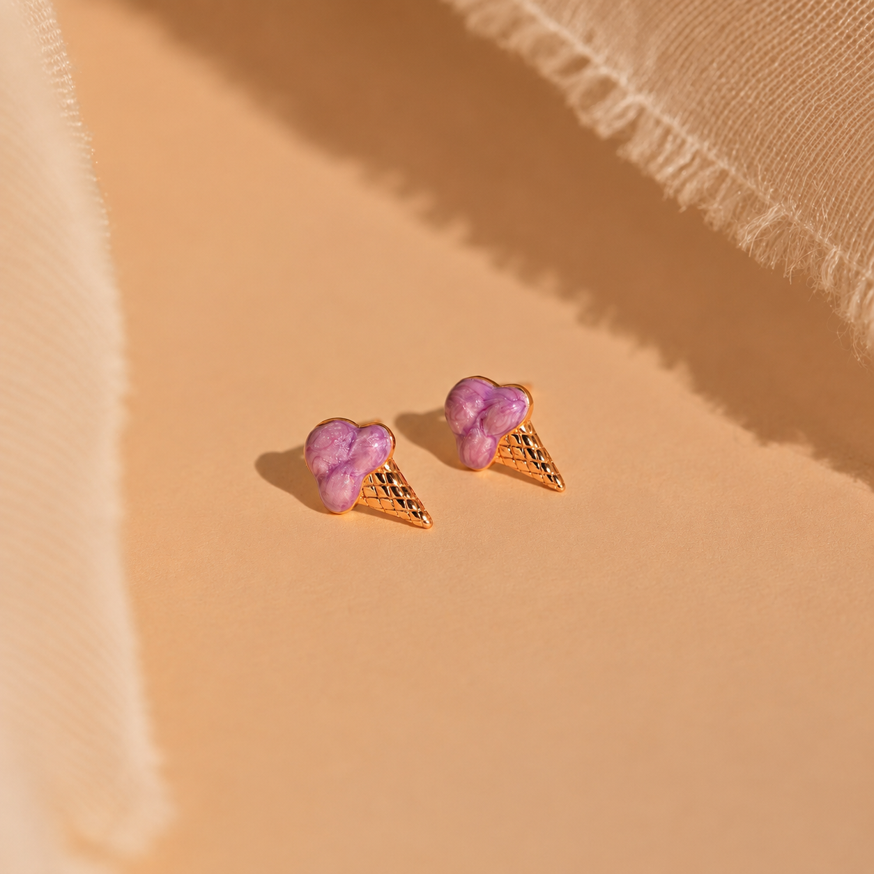 Purple ice cream cone earrings on a beige fabric background