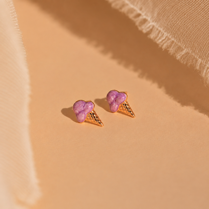 Purple ice cream cone earrings on a beige fabric background