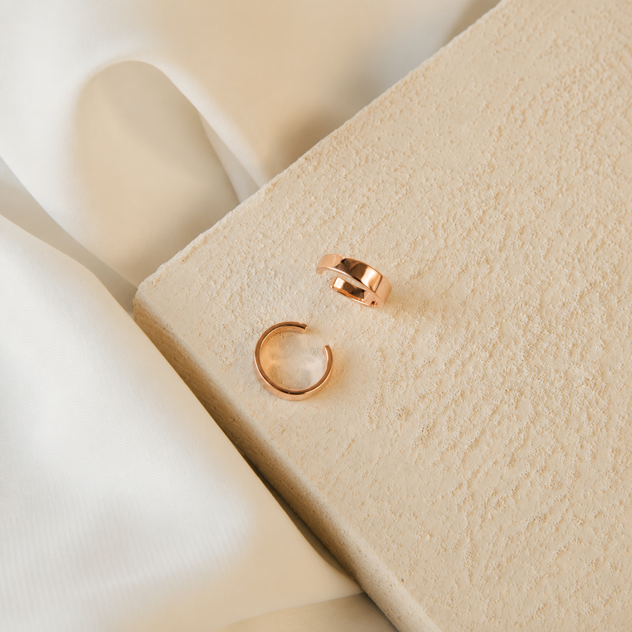 Rose gold hoop earrings on a beige fabric surface