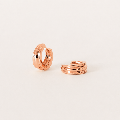Rose gold hoop earring and ring on a light beige background