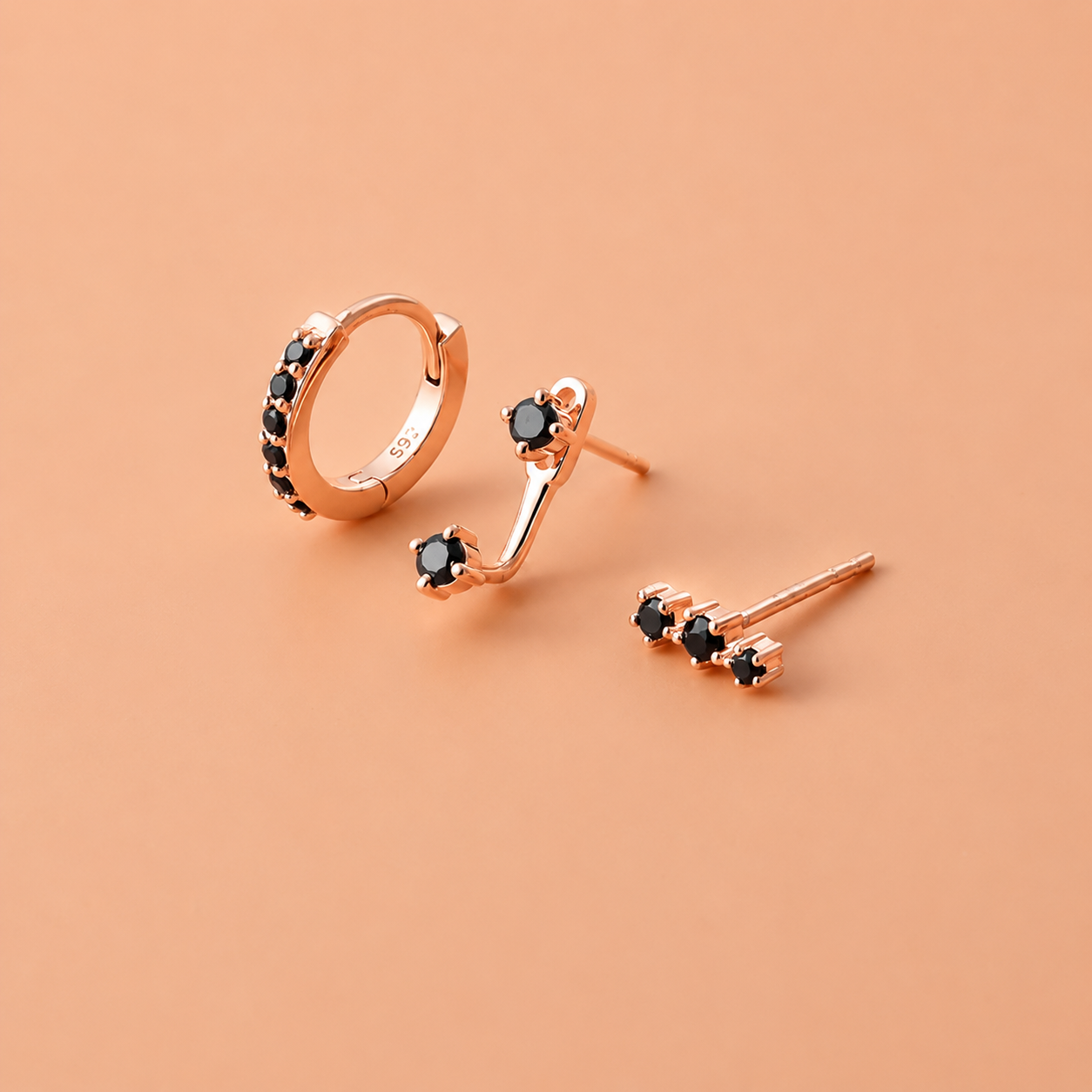 Rose gold earrings with black gemstones on a peach background