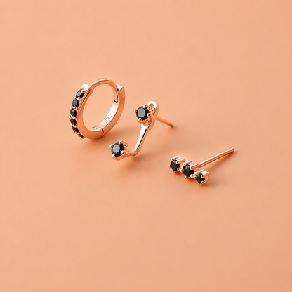 Rose gold earrings with black gemstones on a peach background