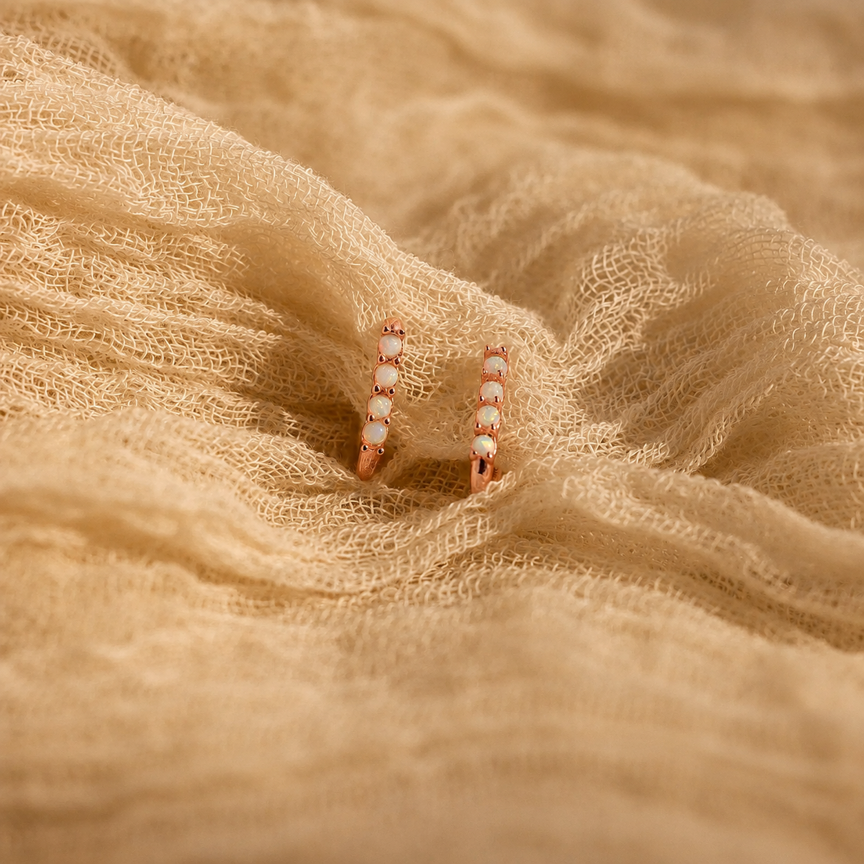 Pair of gold hoop earrings with small pearls on a beige fabric background