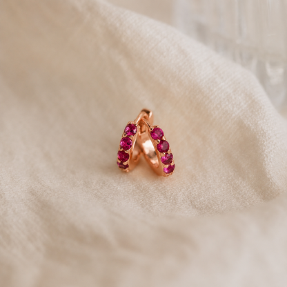 Rose gold earring with red gemstones on a soft beige fabric background