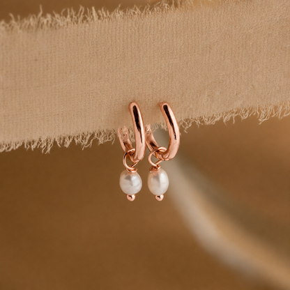 Rose gold hoop earrings with pearl drops on a beige fabric background
