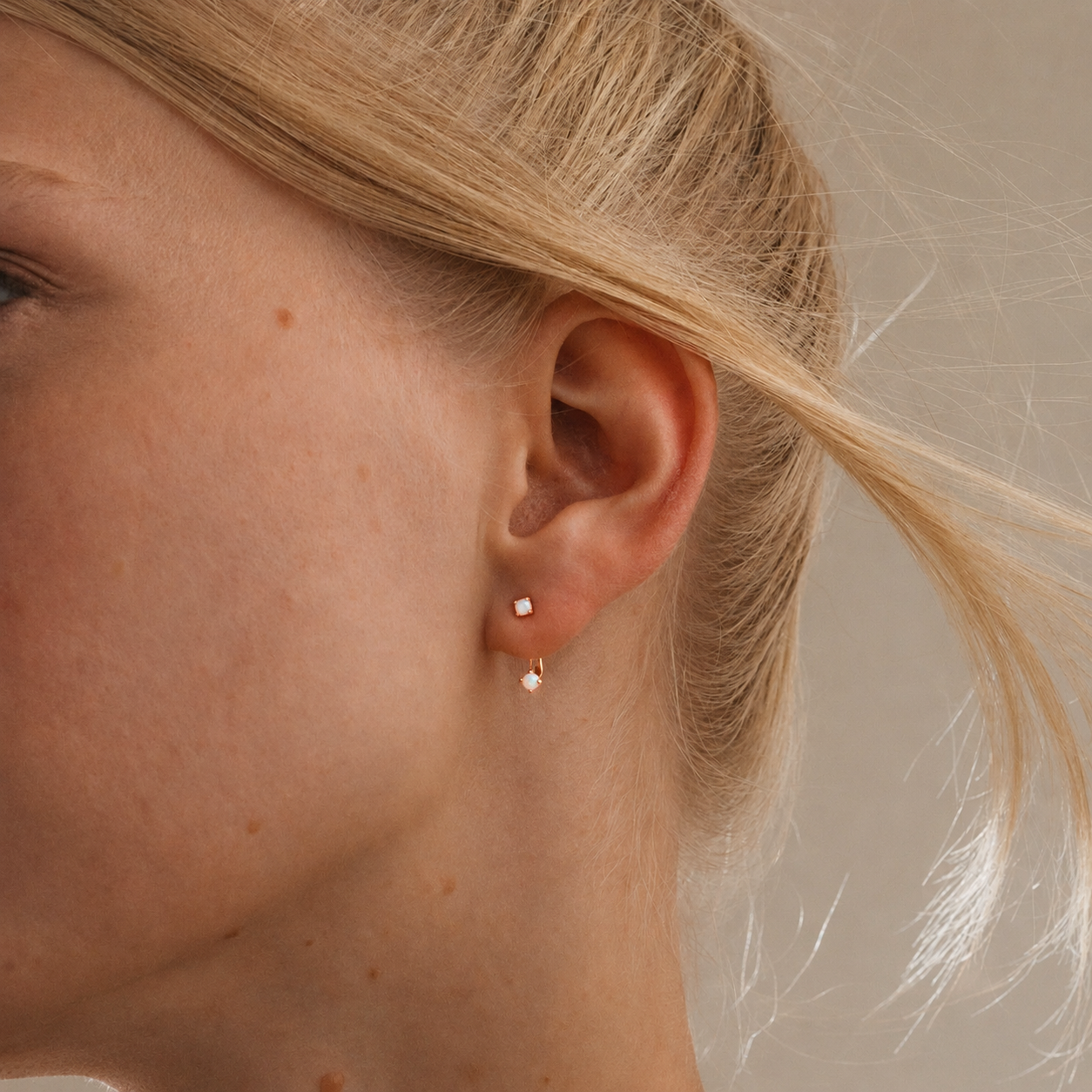 Close-up of a person wearing gold earrings with a neutral background