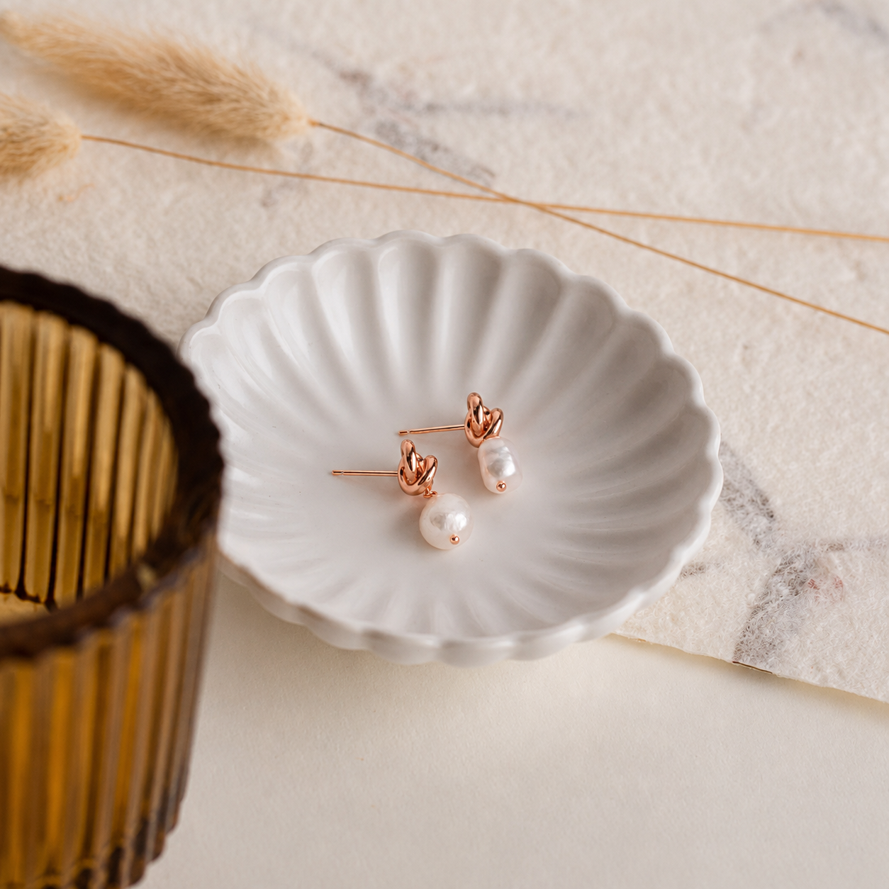 Pearl earrings on a white shell dish with dried plants and a woven basket in the background.