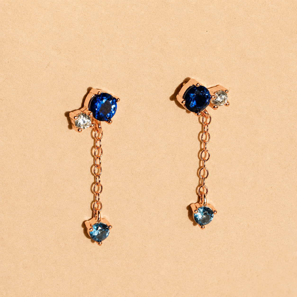 Pair of rose gold earrings with blue gemstones on a beige background