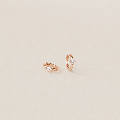 Pair of rose gold hoop earrings with small diamonds on a beige background