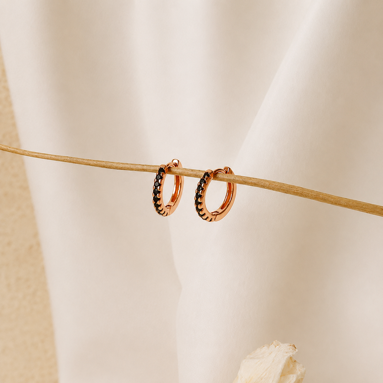 Rose gold hoop earrings with embedded stones on a neutral background