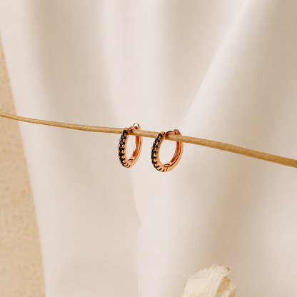 Rose gold hoop earrings with embedded stones on a neutral background