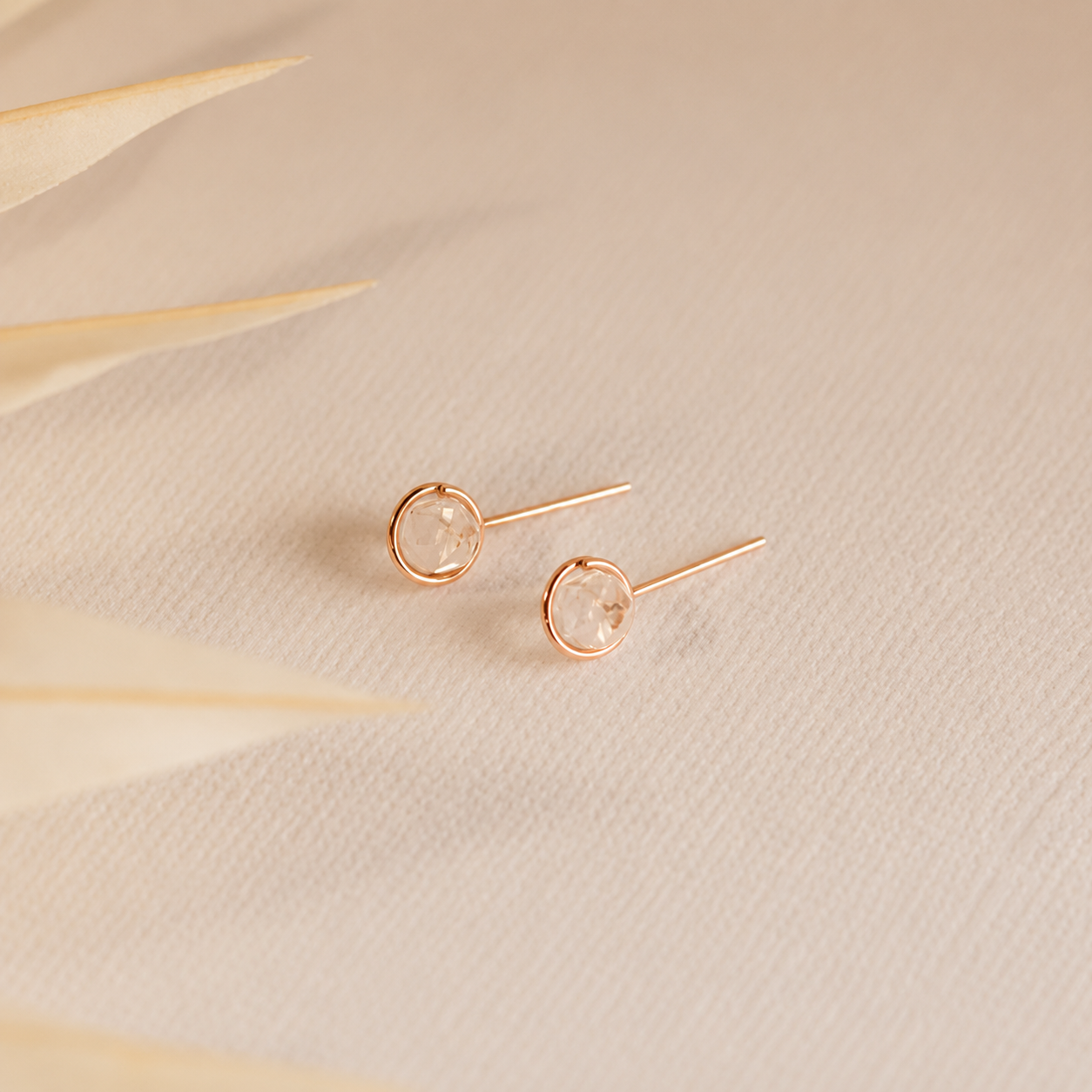 Rose gold earrings on a beige textured surface with dried leaves.