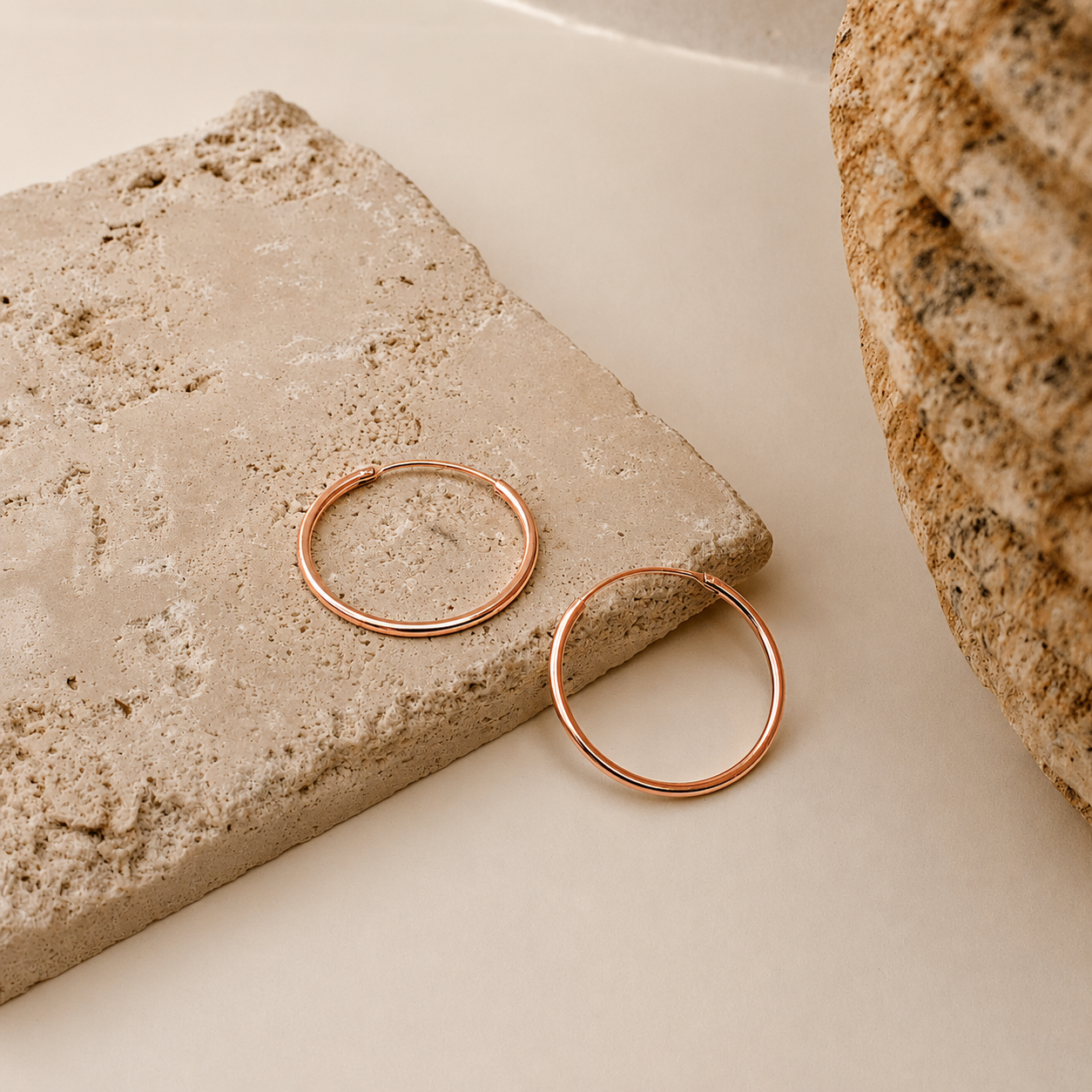 Rose gold hoop earrings on a textured stone surface