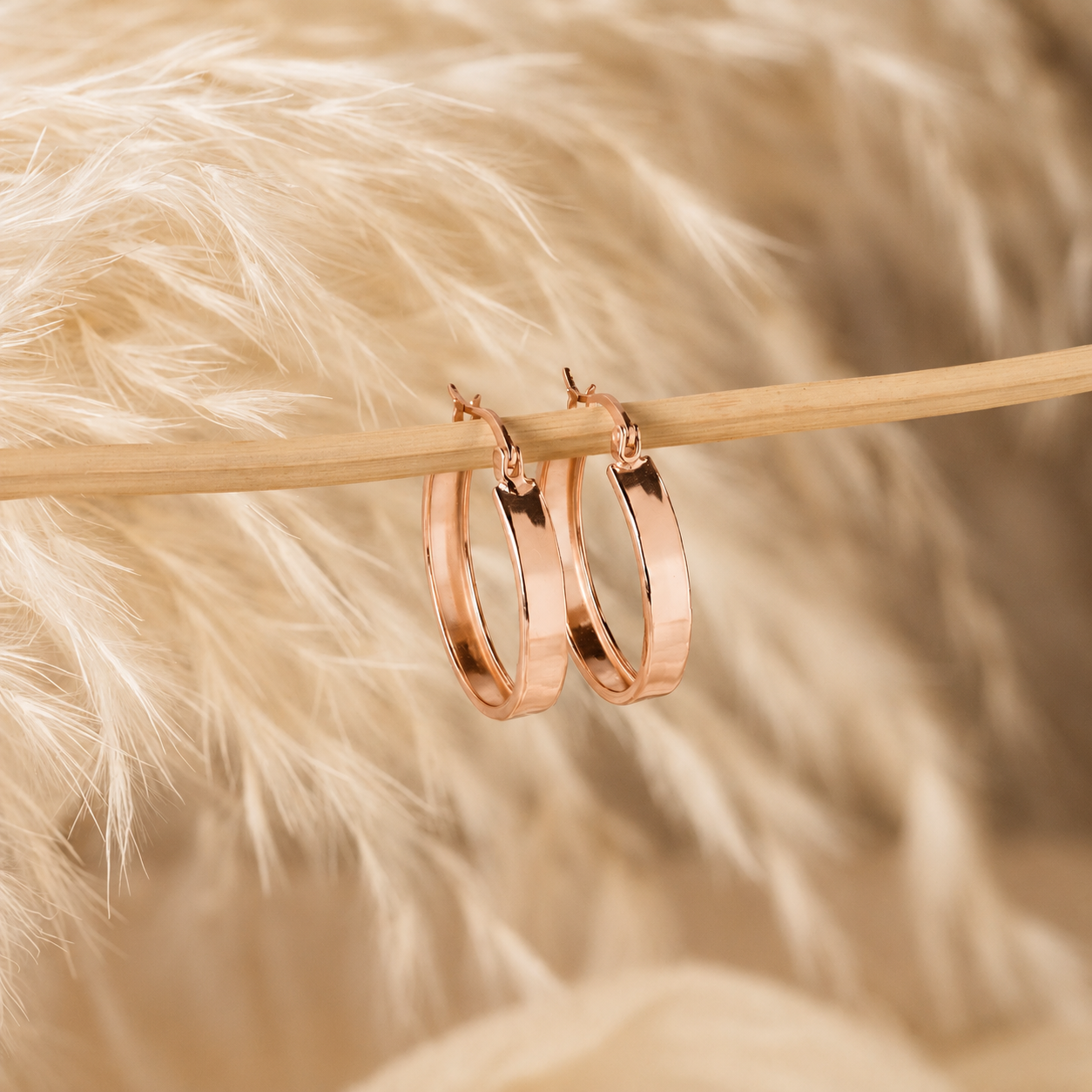 Rose gold hoop earrings on a wooden stick with a soft, blurred background